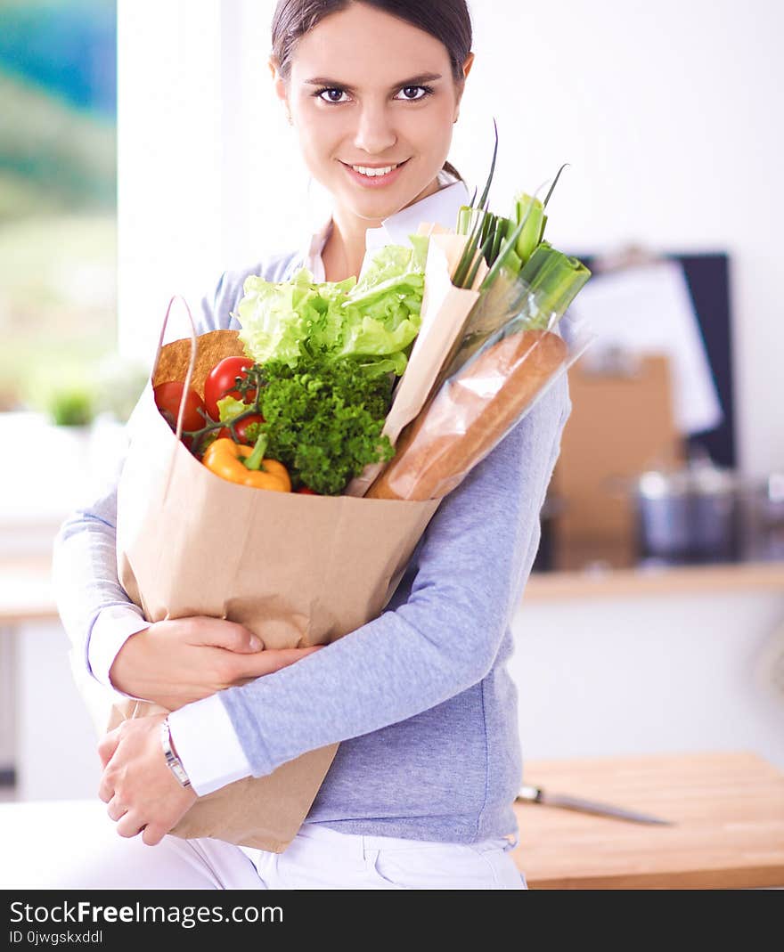 Young woman holding grocery shopping bag with vegetables .Standing in the kitchen