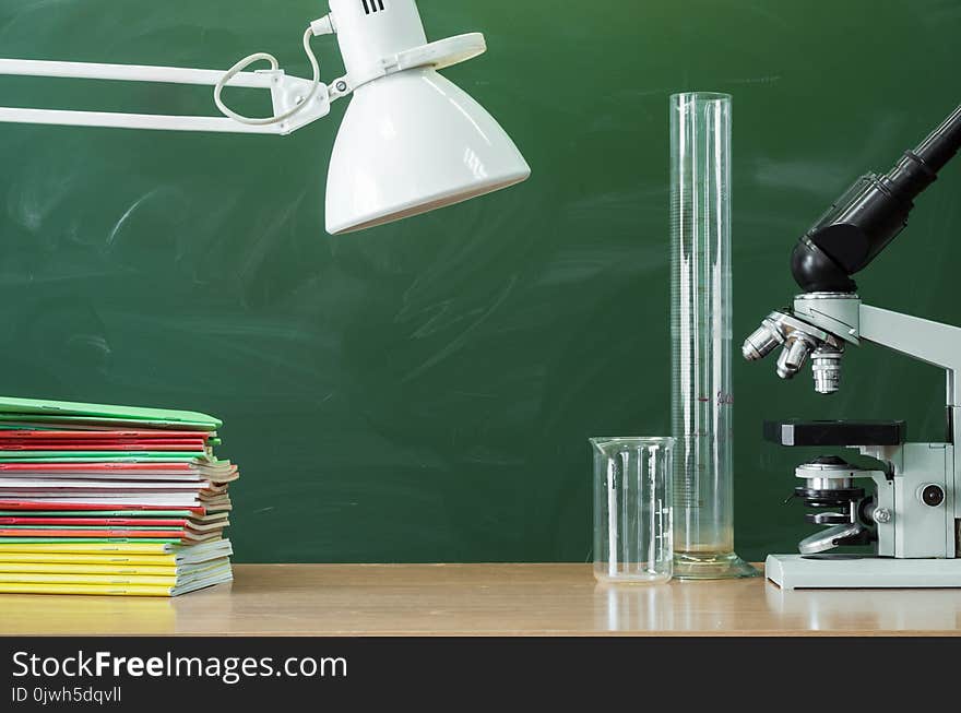 Teacher, student, biologist or chemist desk table. Education background with copy space. Education concept. Microscope, vial, flask, beaker and stacked books on the table. Teacher, student, biologist or chemist desk table. Education background with copy space. Education concept. Microscope, vial, flask, beaker and stacked books on the table.