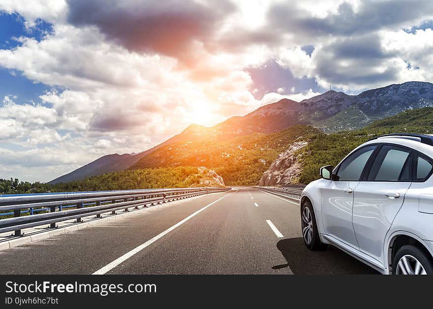 A white car rushing along a high-speed highway in the sun.