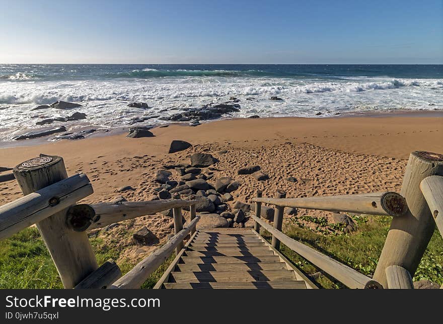 Seascape of empty wooden walkway leading onto rocky beach, waves and sea against blue coastal skyline in South Africa. Seascape of empty wooden walkway leading onto rocky beach, waves and sea against blue coastal skyline in South Africa