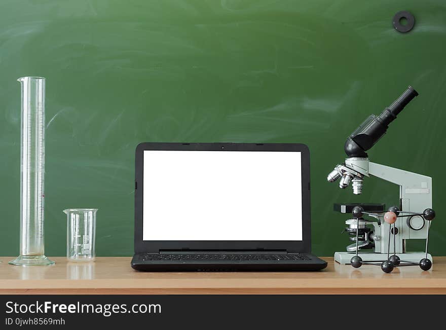 Teacher or student desk table. Education background. Education concept. Laptop with blank screen, microscope, flasks, beaker and molecule model on the table. Chemistry or biology lesson. Teacher or student desk table. Education background. Education concept. Laptop with blank screen, microscope, flasks, beaker and molecule model on the table. Chemistry or biology lesson.