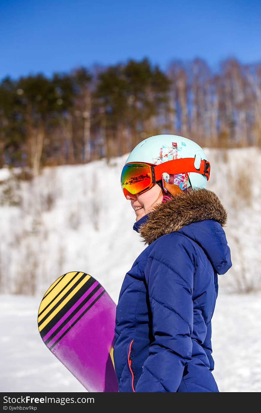 Side view of sporty woman wearing helmet with snowboard looking at camera on winter day