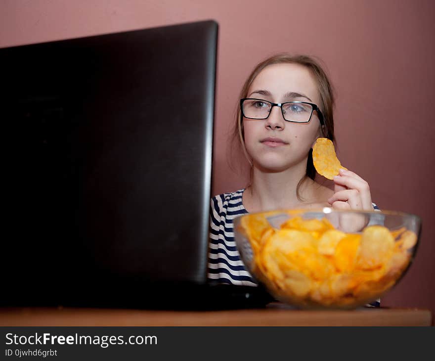 Young happy woman eating chips near a computer. Unhealthy concept