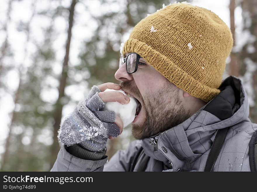 A young bearded man eats a snowball in the forest with pleasure.