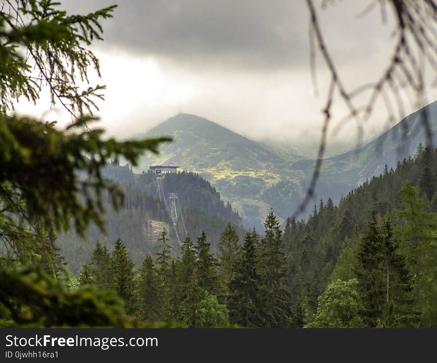 View from route to Nosal peak in Tatras. Forest and trees in the foreground and some peaks of Tatra range in the background. Cable way to Kasprowy Wierch mountain in Poland. Dark cloudy sky and fog . Photo taken during rainy summer day. View from route to Nosal peak in Tatras. Forest and trees in the foreground and some peaks of Tatra range in the background. Cable way to Kasprowy Wierch mountain in Poland. Dark cloudy sky and fog . Photo taken during rainy summer day.