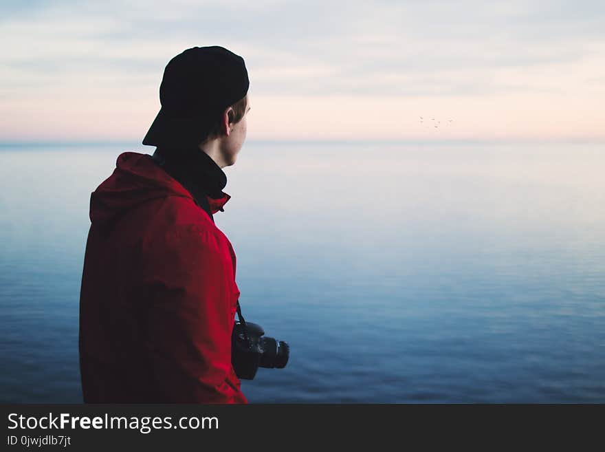 Man in Red Jacket Standing Near Body of Water