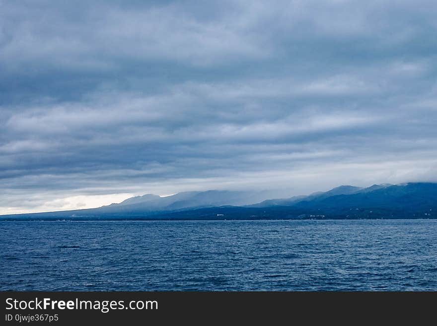 Island Across Body of Water Under Cloudy Sky