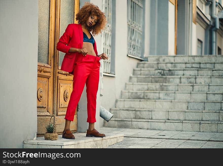 Woman in Black and Blue Sports Bra and Red Pants Standing in Front of Brown Wooden Doors Near Gray Concrete Stairs