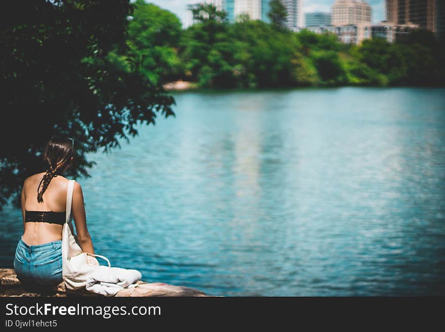 Woman in Black Top Sitting Beside Body of Water