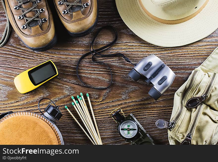 Hiking or travel equipment with boots, compass, binoculars, matches on wooden background. Active lifestyle concept. Top view