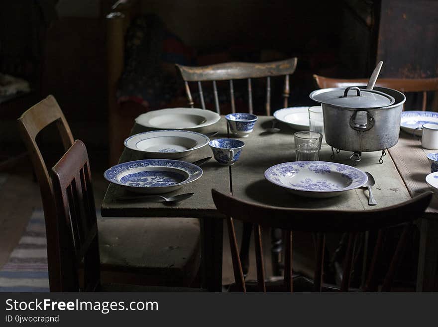 Vintage Set Table With Old Plates And Wooden Chairs In A Poor Interior