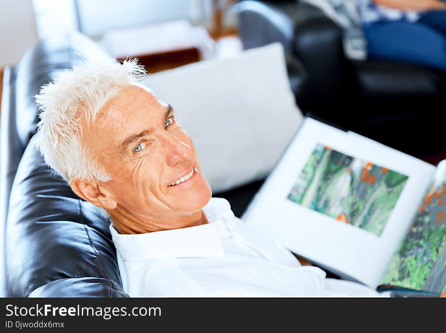 Handsome senior man reading book relaxing on a sofa in the living room at home. Handsome senior man reading book relaxing on a sofa in the living room at home