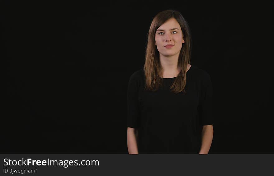 A beautiful young lady smiling and standing with her arms folded against a black background. Medium Shot. A beautiful young lady smiling and standing with her arms folded against a black background. Medium Shot