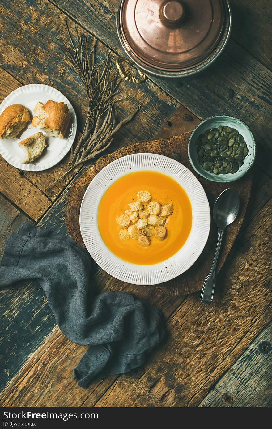 Flat-lay of fall warming pumpkin cream soup with croutons and seeds on board over rustic wooden background, top view, vertical composition. Autumn vegetarian, vegan, healthy comfort food concept. Flat-lay of fall warming pumpkin cream soup with croutons and seeds on board over rustic wooden background, top view, vertical composition. Autumn vegetarian, vegan, healthy comfort food concept