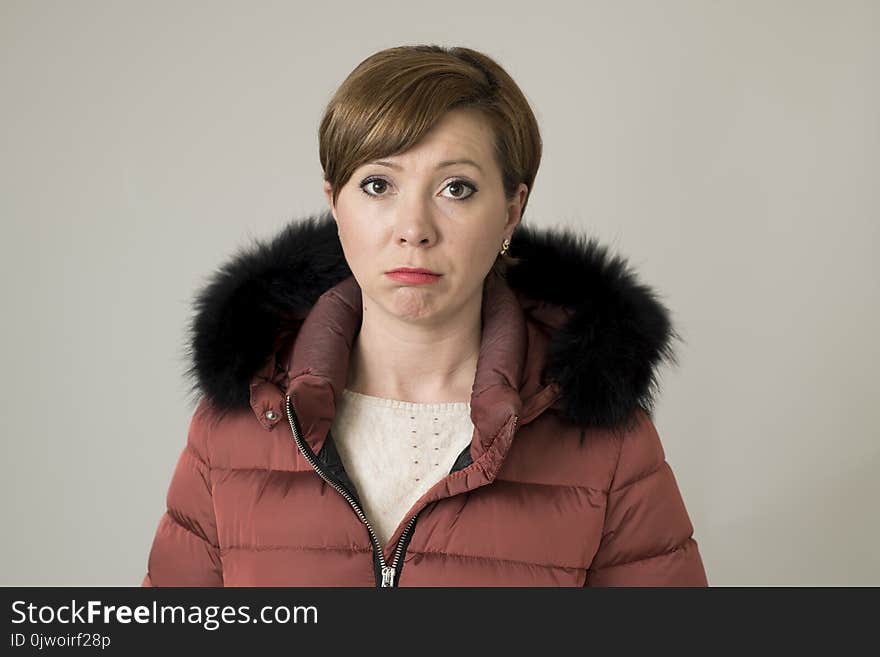 Young sweet and sad red hair woman posing moody and depressed looking to camera wearing warm winter coat jacket with hood isolate