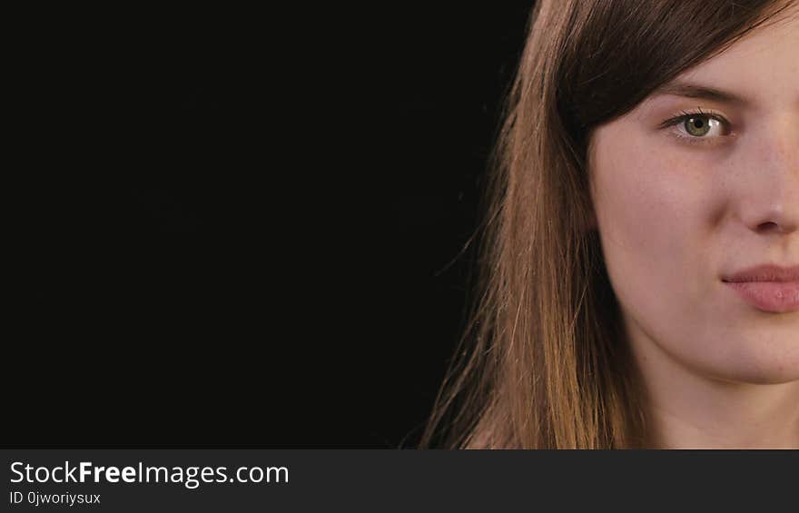 A beautiful young lady`s half face smiling against a black background. Close-up shot. A beautiful young lady`s half face smiling against a black background. Close-up shot