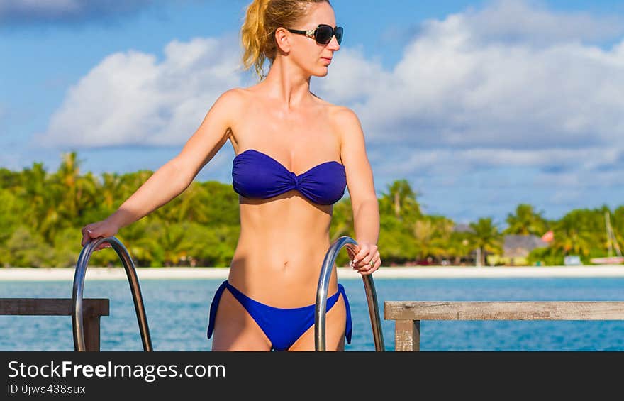 woman in blue bikini wearing sunglasses on a tropical beach background