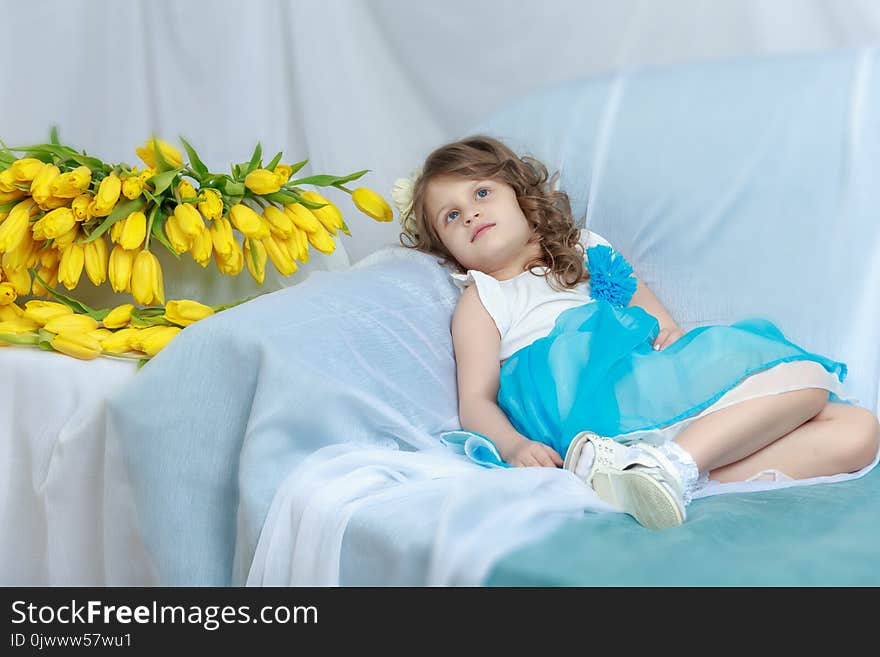 Beautiful little girl sitting on the sofa with a bouquet of yellow tulips. Beautiful little girl sitting on the sofa with a bouquet of yellow tulips.