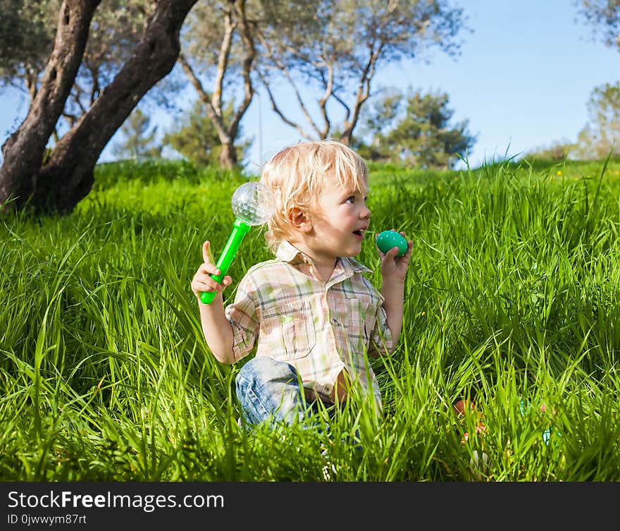 Funny toddler boy pretends to bite a colored Easter egg in the green grass. Funny toddler boy pretends to bite a colored Easter egg in the green grass