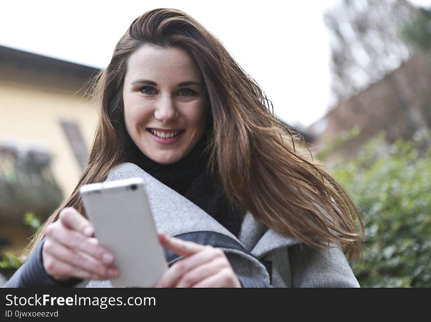 Woman in Gray Coat Holding White Smartphone