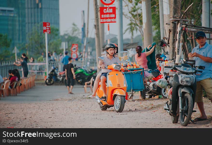 Man Wearing Grey Shirt Riding on Orange Motor Scooter at Daytime