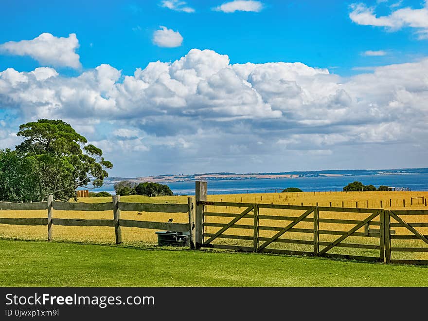 Brown Wooden Fence Across Crop Field Near Body of Water