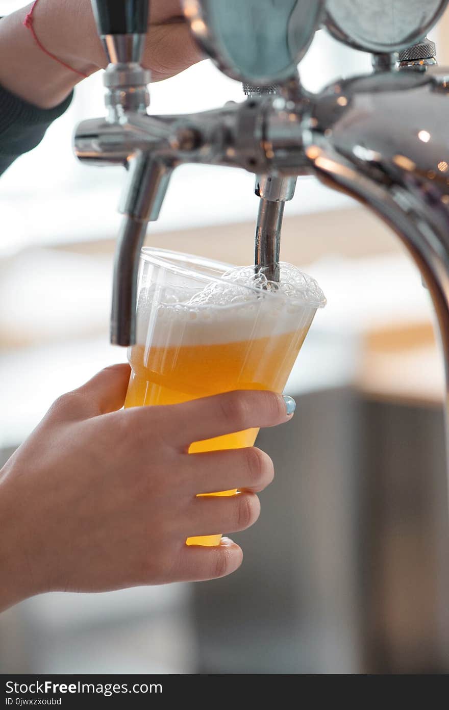 Plastic cup of beer flowing from beer tap with nice foam close-up in female bartender hands