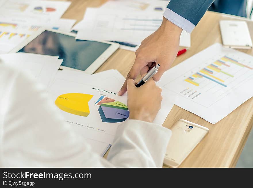 Close-up of business team image of male hand pointing at business document during discussion at meeting and using pen with financial diagram and digital tablet