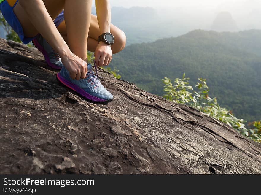 Runner Tying Shoelace On Mountain Top Rock