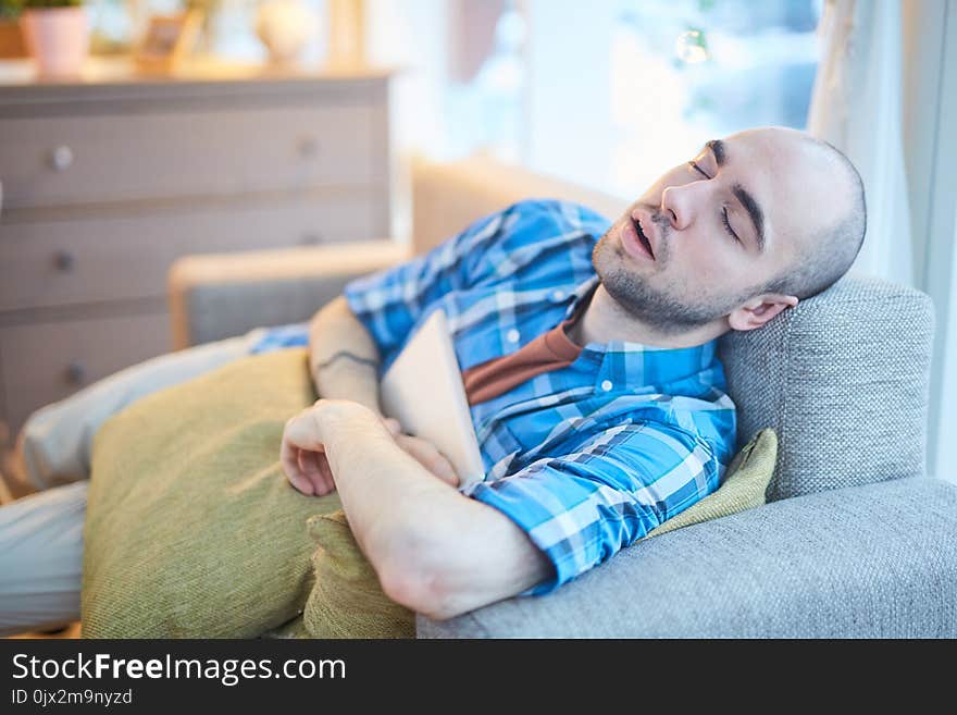 Young man sleeping on sofa with laptop