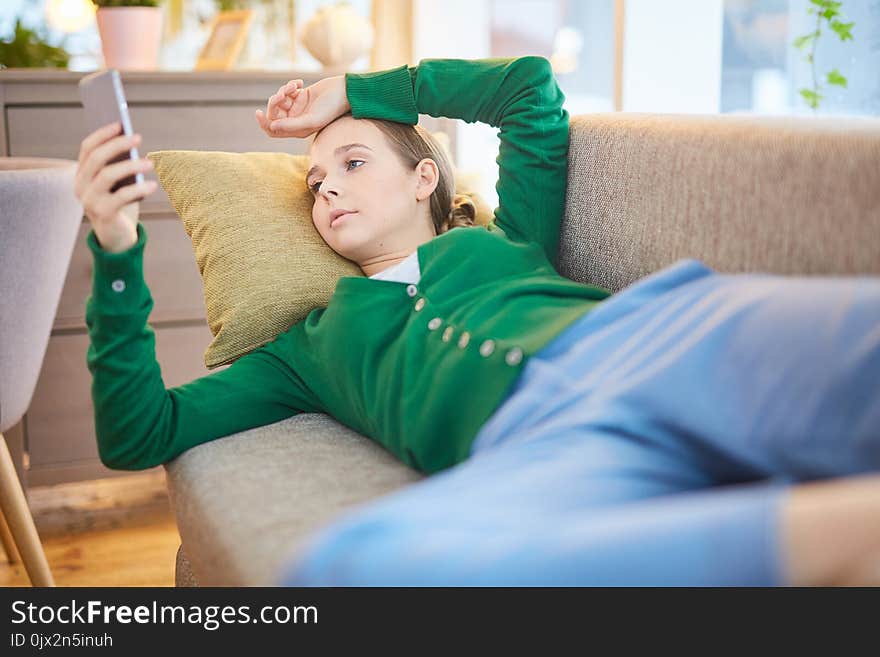 Woman browsing internet on her smartphone lying on the sofa at home. Woman browsing internet on her smartphone lying on the sofa at home