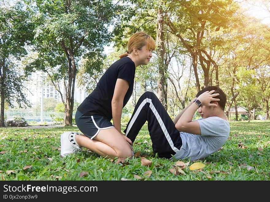 Asian sweet couple exercising together with smile on their faces on soft grass encircle with nature and warm light from the sun in the afternoon. Couple smile happily to each other. Outdoor exercise. Asian sweet couple exercising together with smile on their faces on soft grass encircle with nature and warm light from the sun in the afternoon. Couple smile happily to each other. Outdoor exercise.