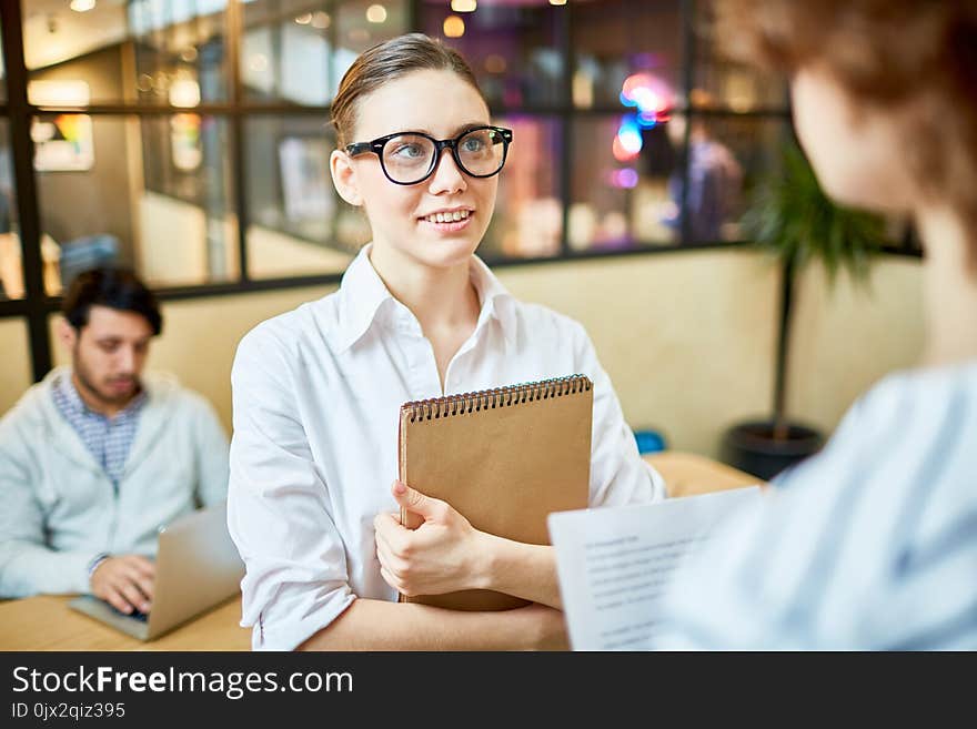 Elegant office worker with notepad listening to her colleague explanation during conversation. Elegant office worker with notepad listening to her colleague explanation during conversation