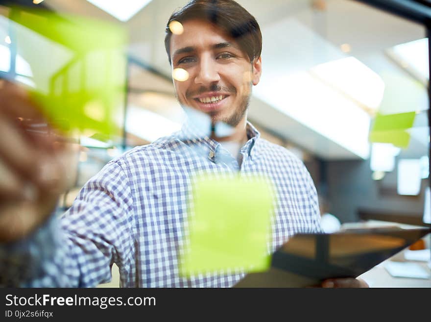 Happy young manager standing by transparent noticeboard with stickers and looking at camera. Happy young manager standing by transparent noticeboard with stickers and looking at camera