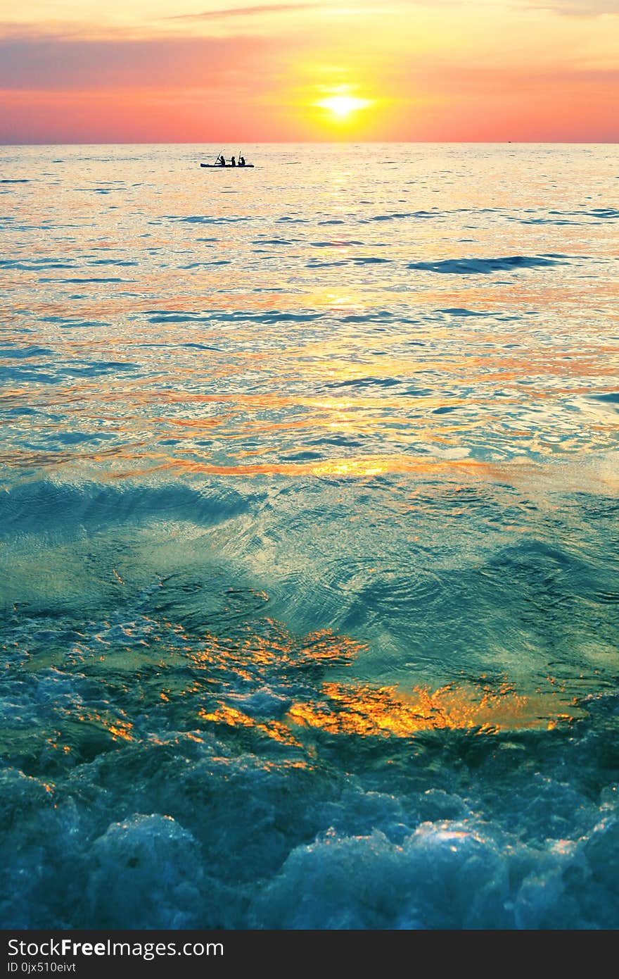 Dramatic colorful sea sunset with sun setting on water lonely boat on horison and dark waves on foreground