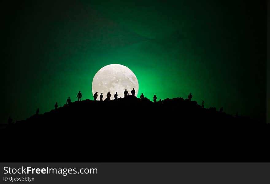 Scary view crowd of zombies on hill with spooky cloudy sky with fog and rising full moon. Silhouette group of zombie walking under