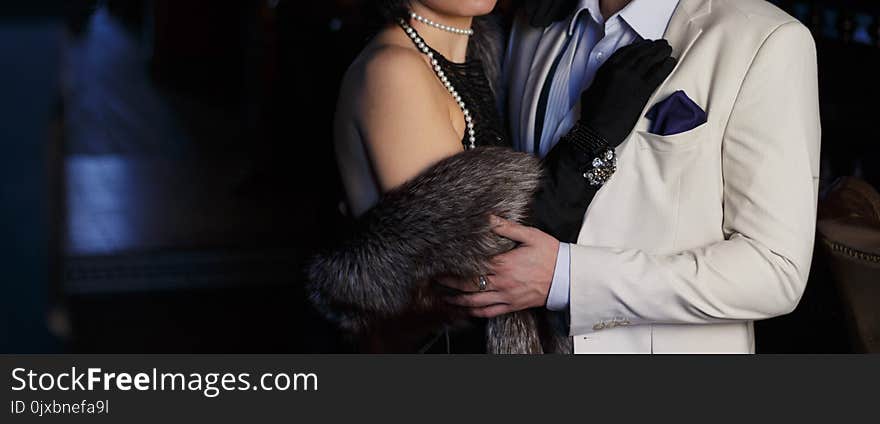 Man in white classic suit hugging woman in evening black dress and fur cape. Man in white classic suit hugging woman in evening black dress and fur cape