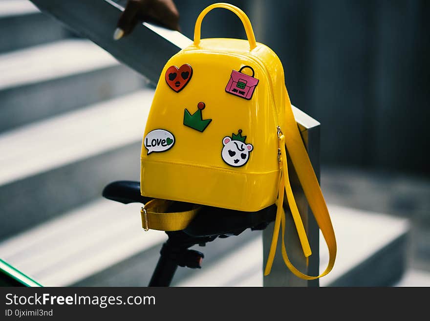 Yellow Backpack With Five Assorted Stickers on Grey Metal Stairway Rail