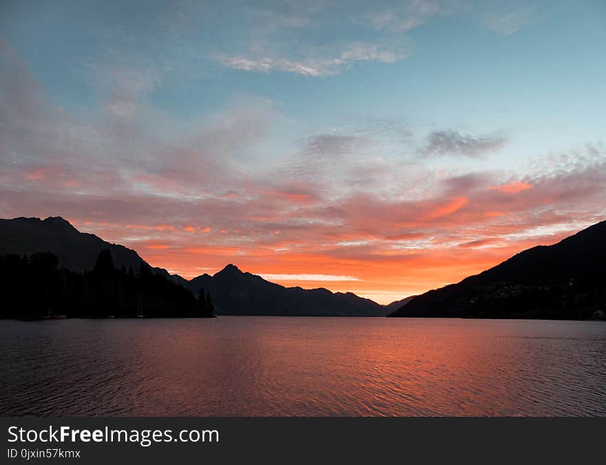 Body of Water Near Silhouette of Mountain Under White Clouds during Sunset