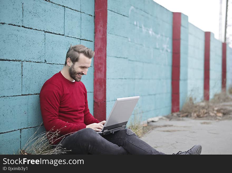 Man Leaning Against Wall Using Laptop