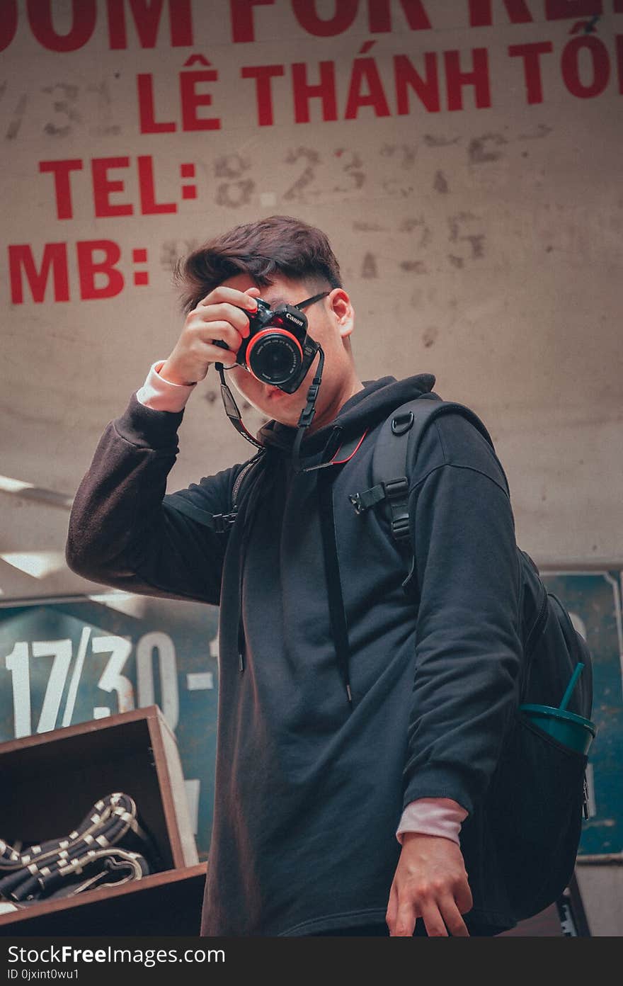 Man Holding Camera Beside Text Printed Wall