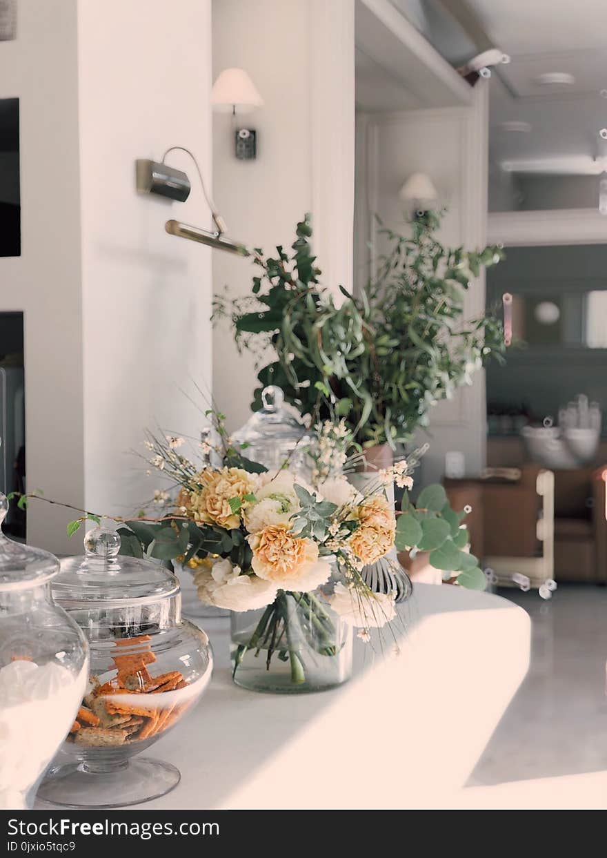 White and Yellow Petaled Flowers Centerpiece Near Clear Glass Jars on Top of White Wooden Table