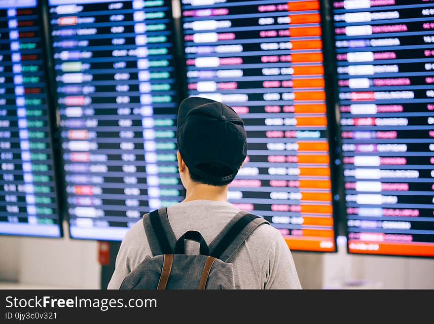 Young male traveler watching and waiting for flight time schedule on boarding time monitor screen.