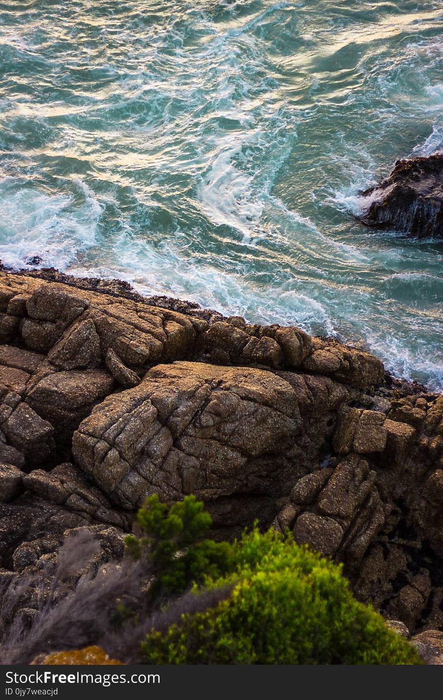 Brown Rock Formation Beside Green Body of Water at Daytime