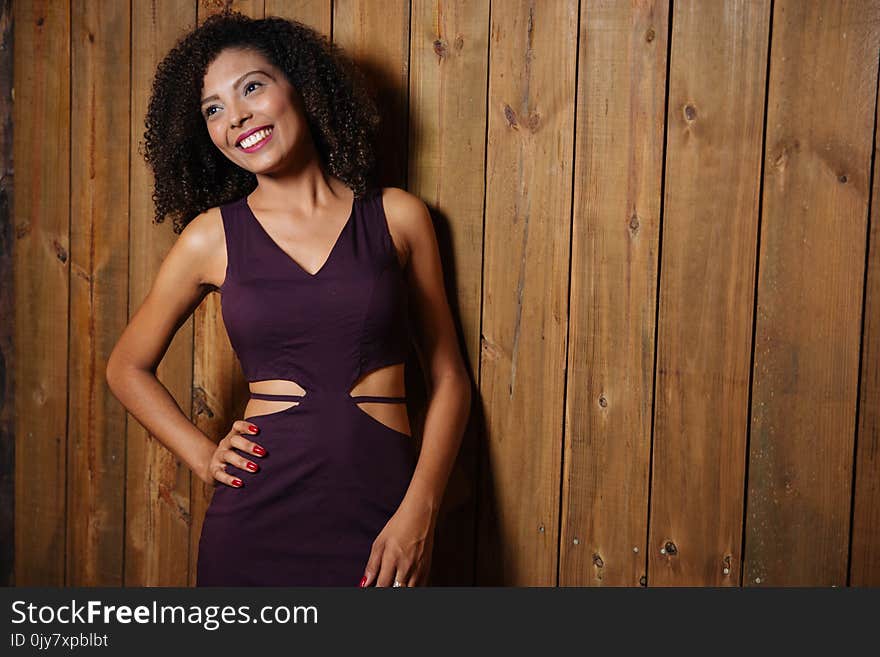 Woman in Purple V-neck Cutout Dress Leaning on Brown Wooden Wall