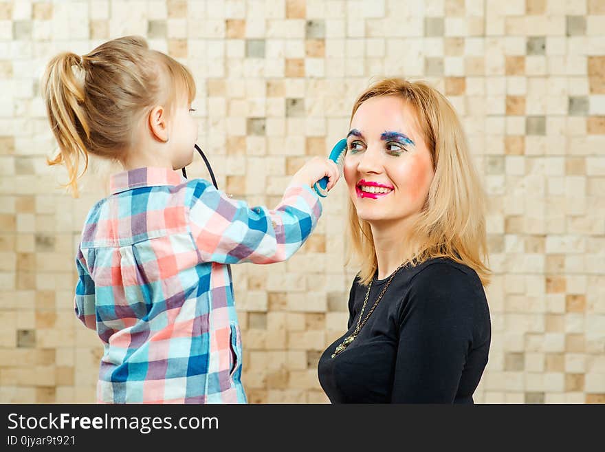 Cute little girl are doing funny make up to her mother at home.