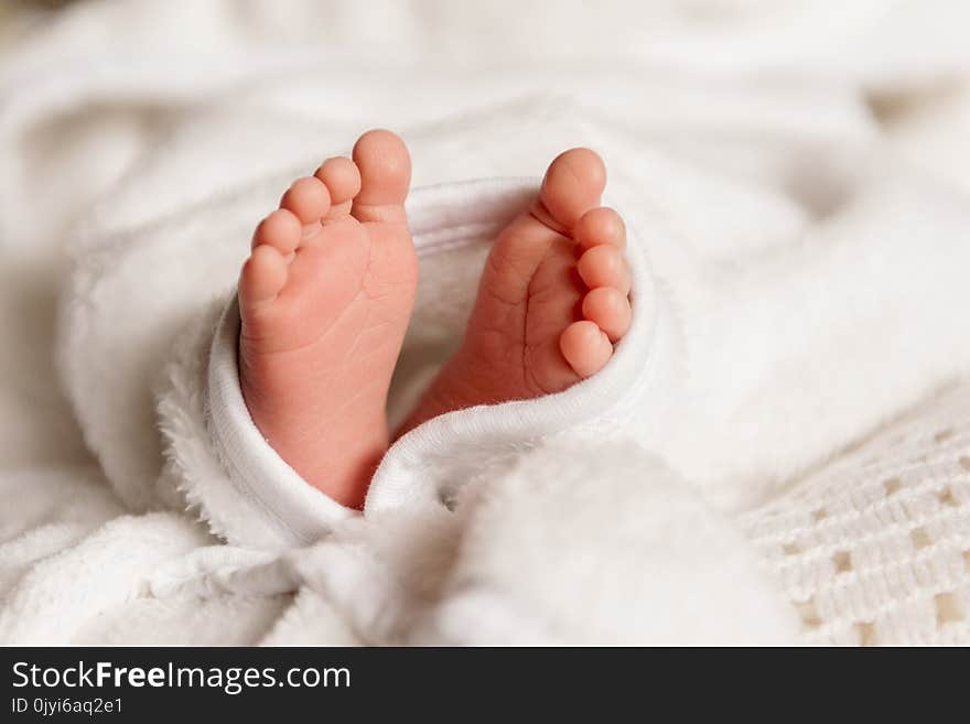 Bare feet of a cute newborn baby in warm white blanket. Childhood. Small bare feet of a little baby girl or boy. Sleeping newborn child.