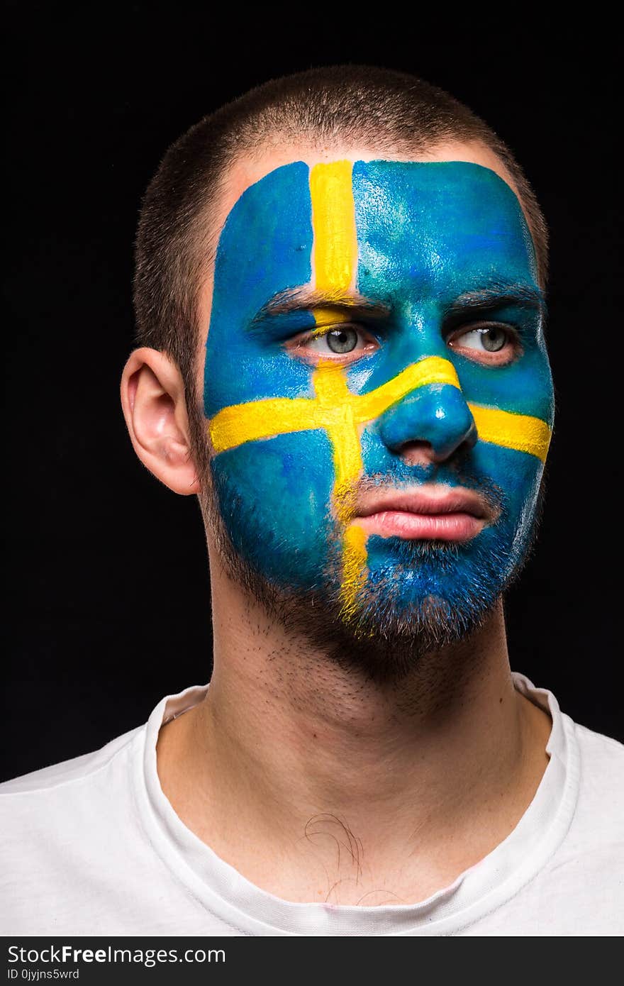 Portrait of handsome man face supporter fan of Sweden national team with painted flag face isolated on black background. Fans emot