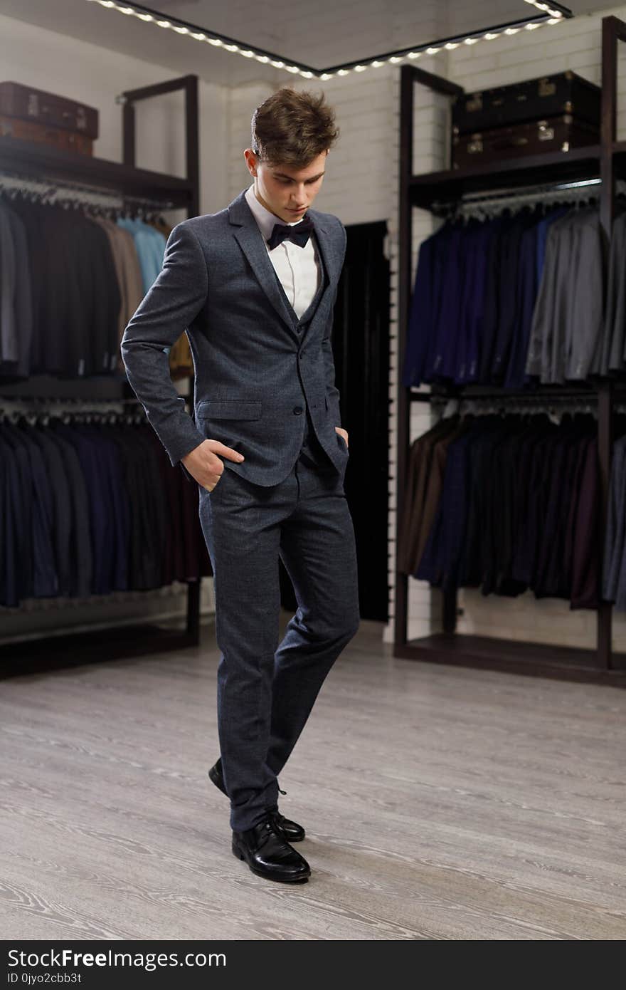 Businessman in classic vest against row of suits in shop. A young stylish man in a jacket. It is in the showroom, trying on clothes, posing. Advertising photo. Businessman in classic vest against row of suits in shop. A young stylish man in a jacket. It is in the showroom, trying on clothes, posing. Advertising photo