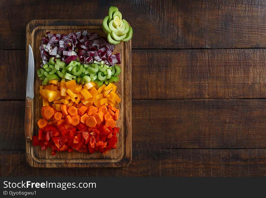 Chopped fresh vegetables arranged on cutting board on dark wooden table with border, top view. Chopped fresh vegetables arranged on cutting board on dark wooden table with border, top view